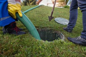 Two people standing in the grass pumping a septic tank.