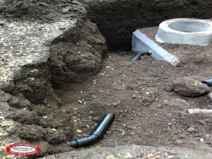 black pipe in a dug hole being covered with dirt