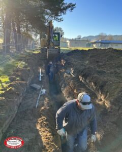 Two Men in a Ditch With a Large Digger at the End.