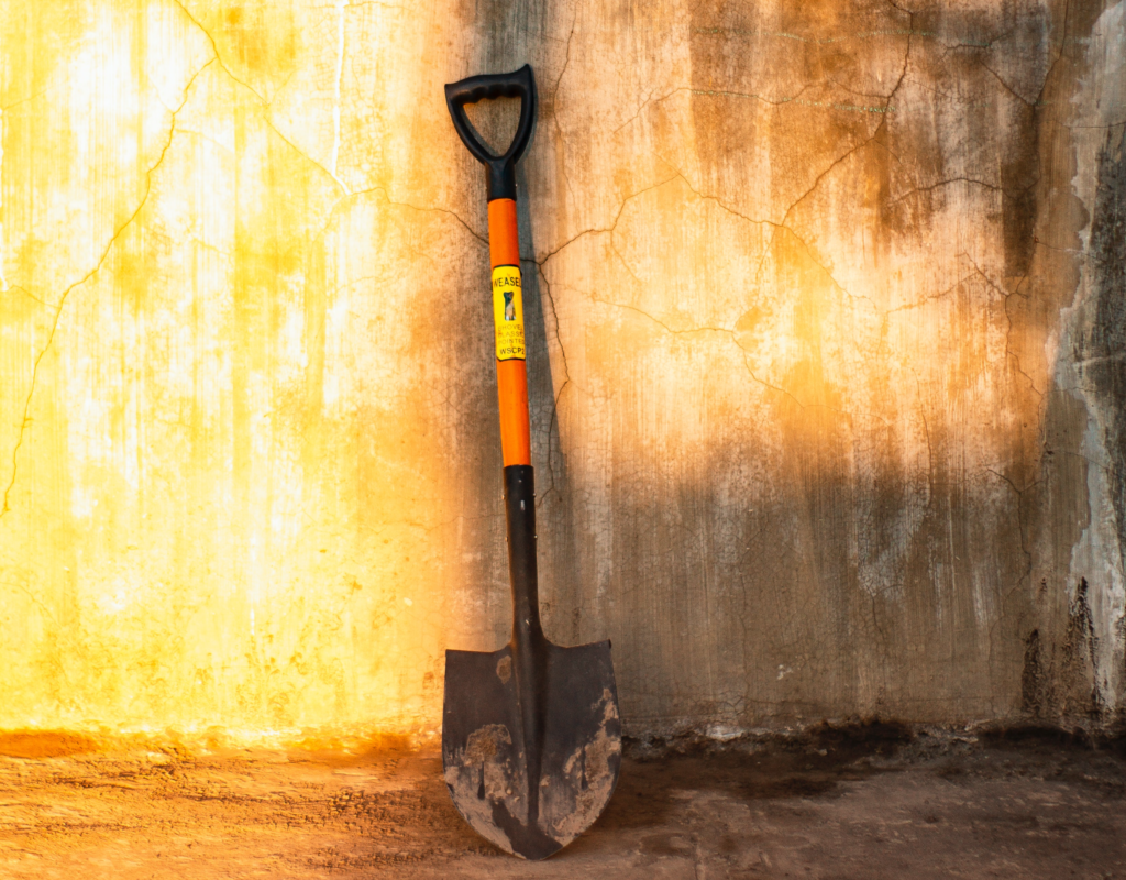 metal spade leaning against a weathered wall in the sunlight