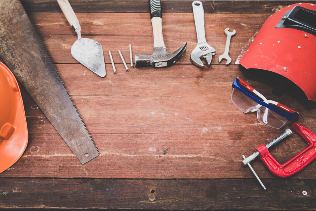 hand tools including hammer, saw and helmet laid out on wooden board