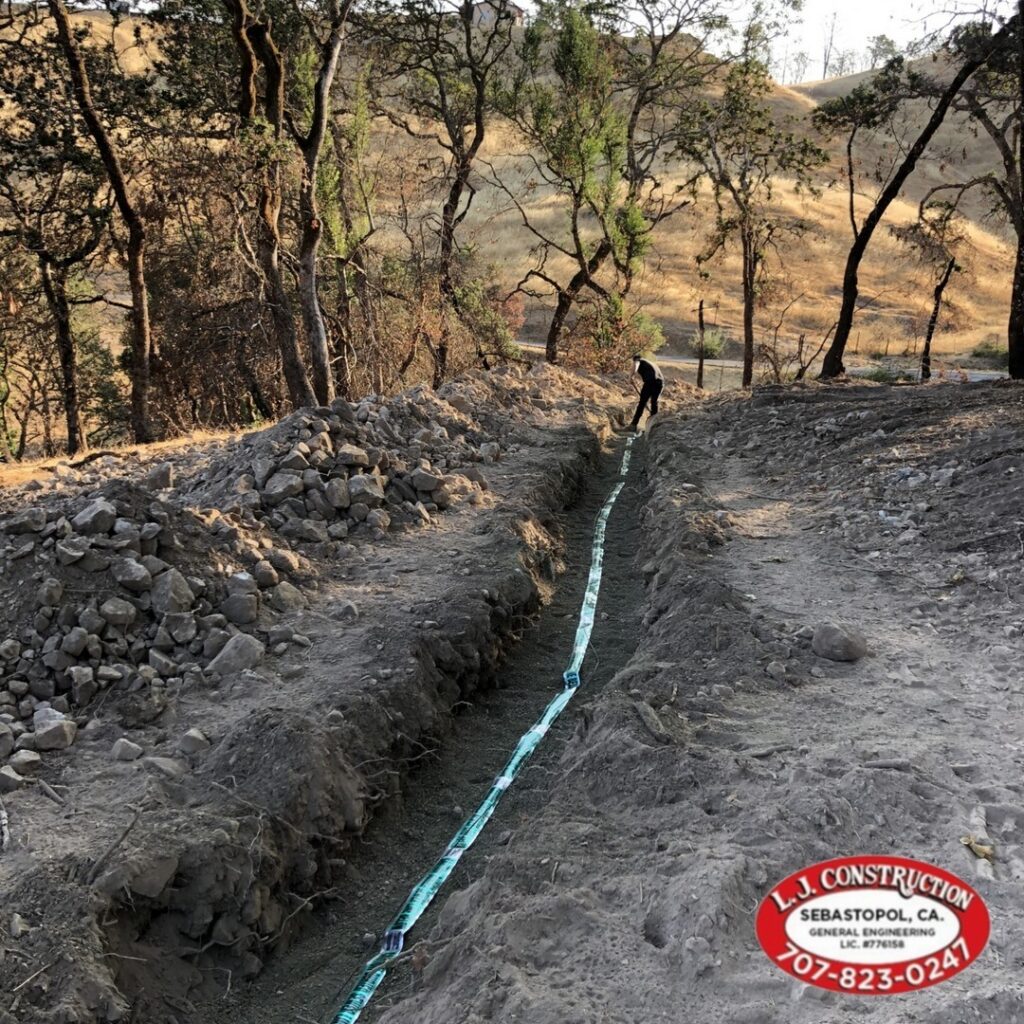 Long dug-out dirt path with rocks on either side and a man working at the end