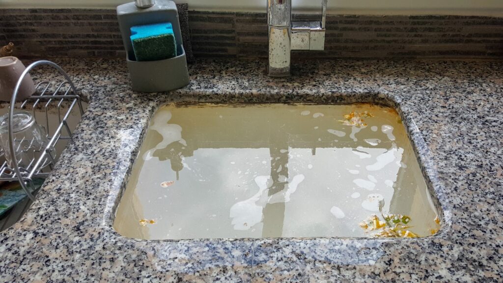 A clogged sink is filled to the brim with dirty water.