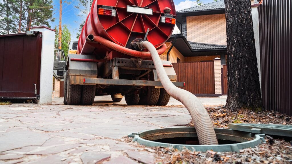 A septic tank truck with a large hose extended from it into an open septic tank opening.