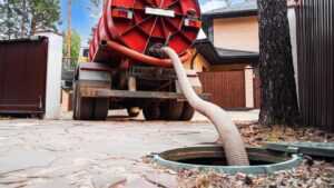 A septic tank truck with a large hose extended from it into an open septic tank opening.