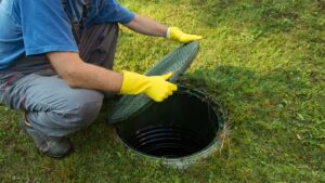 A man in yellow protective gloves uncovers the lid on a septic tank.