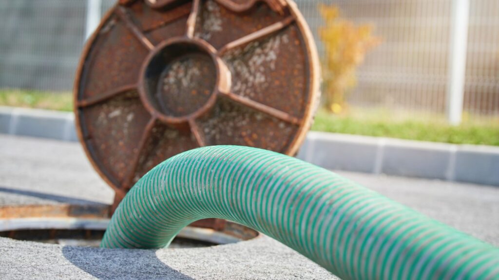 A large green hose for pumping septic lowered into a septic tank opening.