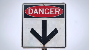 A white sign with a black arrow pointing down, a red circle above says “DANGER”.